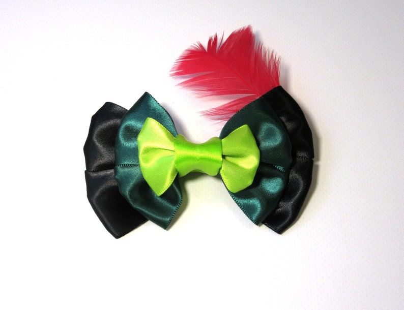 Puede incluir: Un lazo verde, negro y verde oscuro con un centro verde lima y un acento de pluma roja.