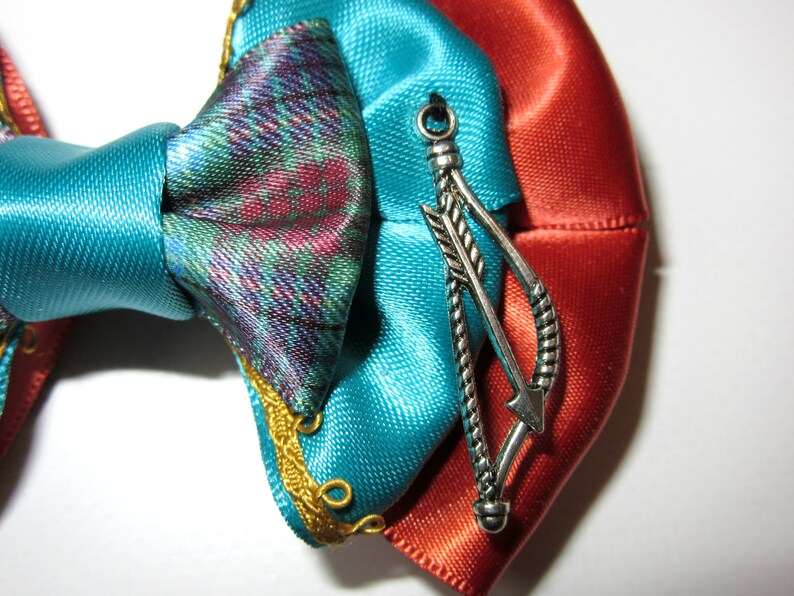 May include: A turquoise and orange satin bow with a silver arrow charm. The bow has gold trim and is tied with a knot.