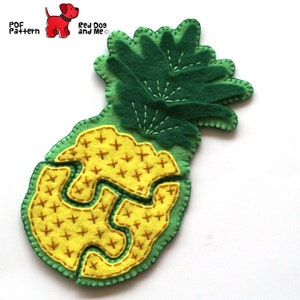 May include: A felt pineapple with a green top and yellow body. The pineapple is divided into sections with a zig-zag pattern. The pineapple is decorated with yellow stitches in the shape of plus signs.