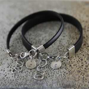 May include: Two black leather bracelets with silver clasps and charms. The charms are round and have the letters "N" and "S" engraved on them.