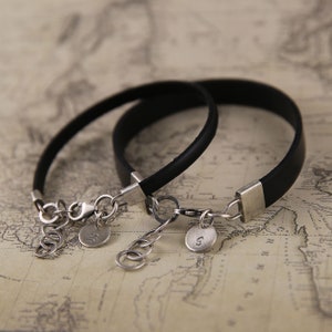 May include: Two black leather bracelets with silver clasps and charms. The charms are engraved with the letters "J" and "S".