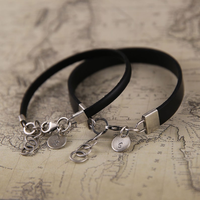 May include: Two black leather bracelets with silver clasps and charms. The charms are engraved with the letters "J" and "S".