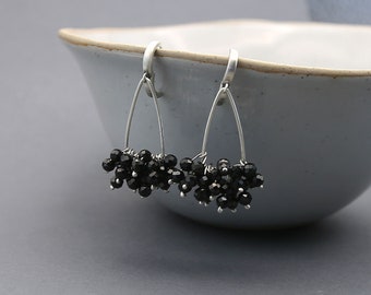 May include: A pair of silver dangle earrings with black gemstone beads hanging from a teardrop-shaped wire frame.