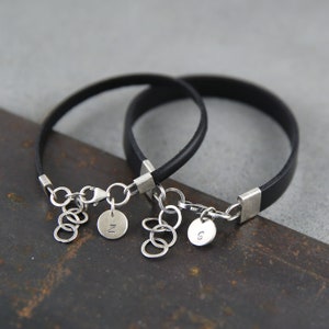 May include: Two black leather bracelets with silver clasps and charms. The charms are round and have the letters "N" and "S" engraved on them.