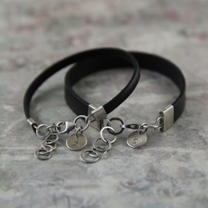 May include: Two black leather bracelets with silver clasps and charms. The charms are round and have the letters "N" and "S" engraved on them.
