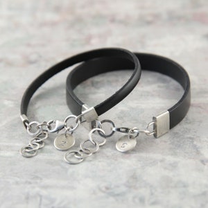May include: Two black leather bracelets with silver clasps and charms. The charms are round and engraved with the letters "J" and "S".