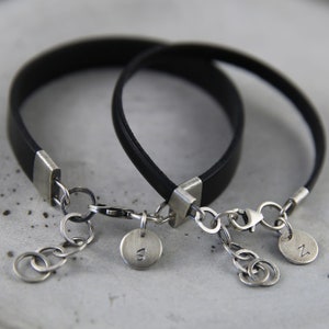 May include: Two black leather bracelets with silver clasps and charms. The charms are round and have the letters "N" and "W" engraved on them.