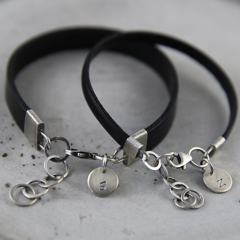 May include: Two black leather bracelets with silver clasps and charms. The charms are round and have the letters "N" and "W" engraved on them.