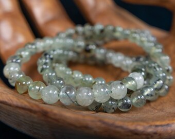 May include: A set of three green and black gemstone bracelets. The bracelets are made of round beads and are stacked on top of each other.