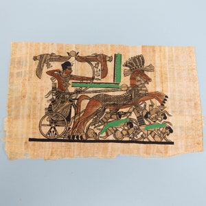 Può includere: Un rotolo di papiro dipinto a mano che raffigura un faraone egizio che guida un carro trainato da un cavallo. Il faraone indossa una corona e tiene un arco e una freccia. Il carro è decorato con dettagli intricati e il cavallo è adornato con un copricapo piumato. Il rotolo è incorniciato da un bordo di geroglifici.