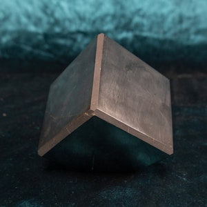 May include: A dark gray, geometric, triangular-shaped object with sharp edges and a smooth surface.