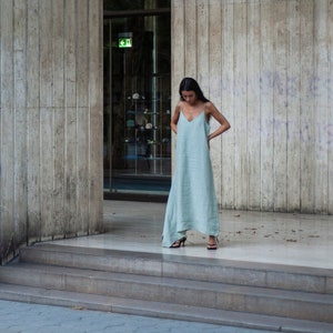 May include: A woman in a light blue maxi dress stands in front of a building with the text "Borsa de Barcelona" on the side. The building has a concrete facade and a large glass door.