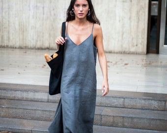 May include: A woman wearing a gray linen dress and black sandals carries a black tote bag with a baguette inside. She is walking down a set of stairs.