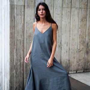 May include: A woman wearing a gray maxi dress with a V-neckline and thin straps. The dress has a flowing, asymmetrical hemline.