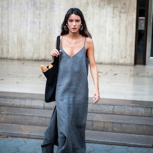 May include: A woman wearing a gray linen dress and black sandals carries a black tote bag with a baguette inside. She is walking down a set of stairs.