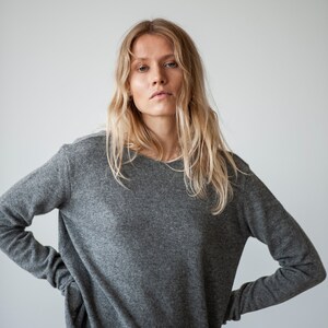 May include: A woman wearing a gray long-sleeved sweater with a relaxed fit. The sweater has a slightly oversized look and is made of a soft, comfortable fabric.