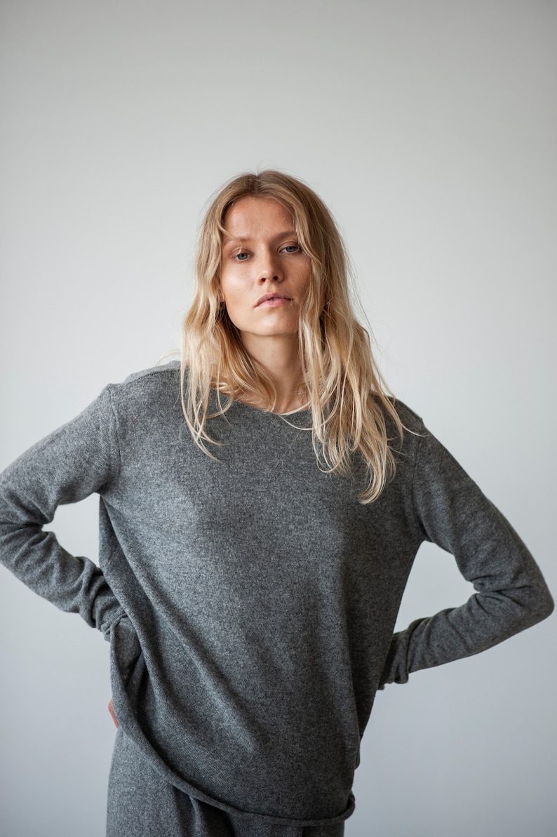May include: A woman wearing a gray long-sleeved sweater with a relaxed fit. The sweater has a slightly oversized look and is made of a soft, comfortable fabric.