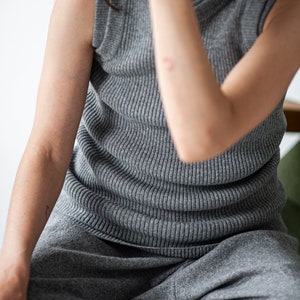 Op de afbeelding: Een grijs, mouwloos, geribbeld gebreid topje en een bijpassende grijze joggingbroek. Het topje heeft een hoge halslijn en de broek heeft een ontspannen pasvorm.