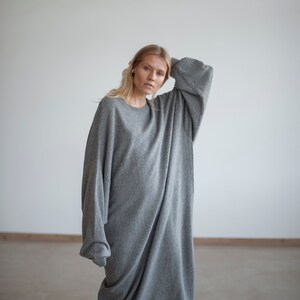 May include: A woman wearing a long, gray, oversized sweater dress. The sweater is made of a soft, knit fabric and has a relaxed fit.