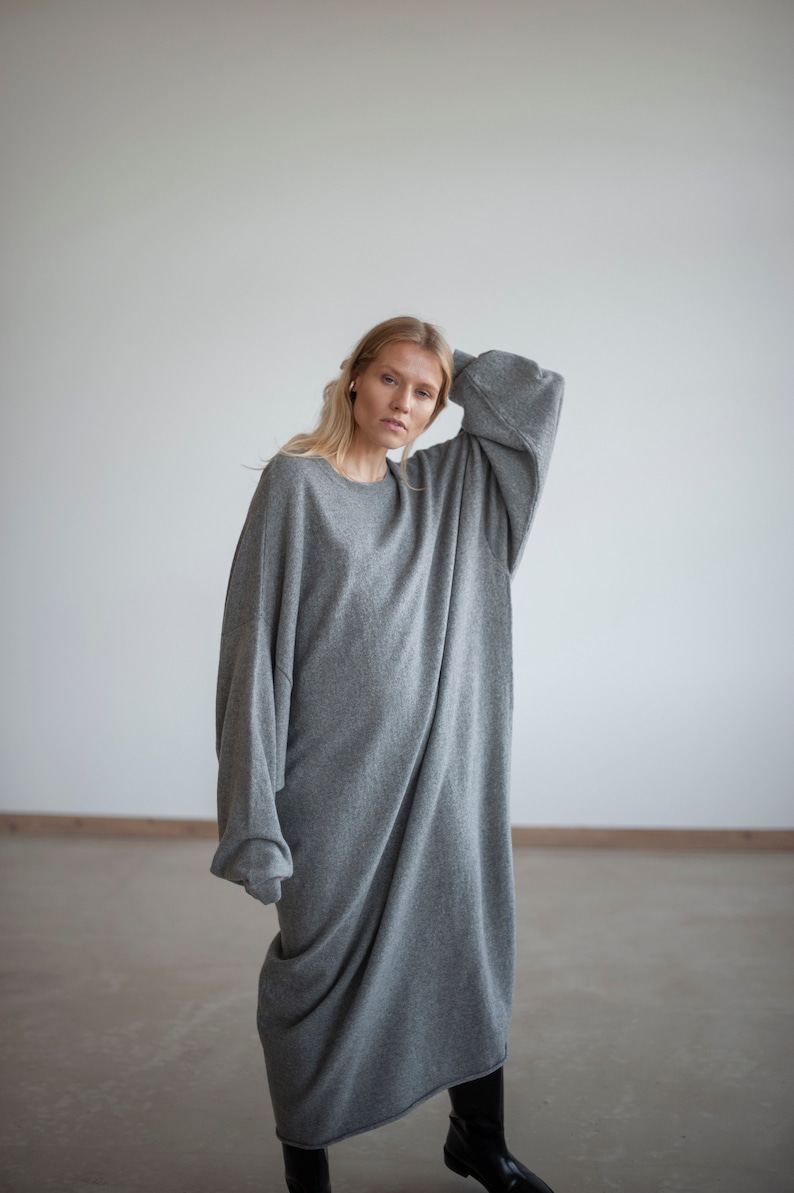 May include: A woman wearing a long, gray, oversized sweater dress. The sweater is made of a soft, knit fabric and has a relaxed fit.
