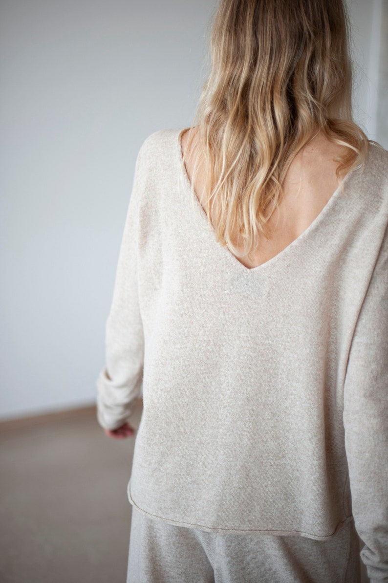 May include: A light beige long-sleeved sweater with a deep V-neck. The sweater is made of a soft, comfortable fabric and has a relaxed fit.
