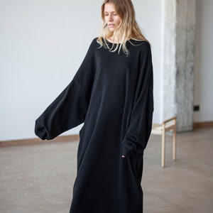 May include: A long black oversized sweater dress with long sleeves and a round neckline.