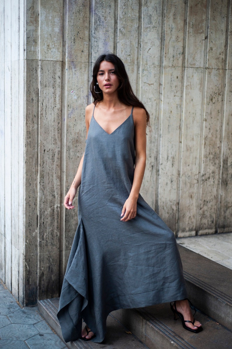 May include: A woman wearing a gray maxi dress with a V-neckline and thin straps. The dress has a flowing, asymmetrical hemline.