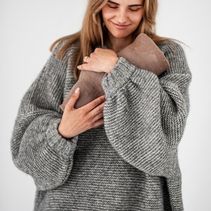 May include: A woman wearing a gray knitted sweater is holding a brown leather clutch purse.