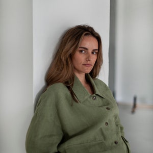 K&ouml;nnte beinhalten: Eine Frau tr&auml;gt ein gr&uuml;nes Leinenhemd mit Kragen und Knopfleiste. Das Hemd hat eine aufgesetzte Tasche auf der linken Seite und ist leicht oversized.