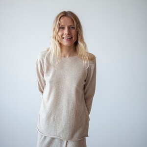 May include: A woman wearing a light beige sweater and matching skirt. The sweater has long sleeves and a relaxed fit. The skirt is a-line and falls to her knees.