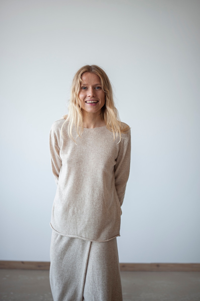 May include: A woman wearing a light beige sweater and matching skirt. The sweater has long sleeves and a relaxed fit. The skirt is a-line and falls to her knees.