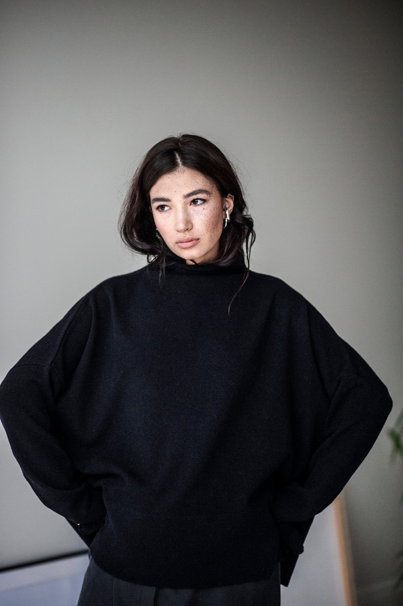 May include: A woman wearing a black mock neck sweater with long sleeves. The sweater has a relaxed fit and is made of a soft, comfortable material.