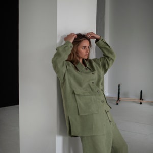 K&ouml;nnte beinhalten: Eine Frau tr&auml;gt einen gr&uuml;nen Leinen-Jumpsuit mit einem Hemdkragen und einer gro&szlig;en Tasche auf der Vorderseite. Der Jumpsuit hat eine lockere Passform und ist mit einem l&auml;ssigen Look gestylt.