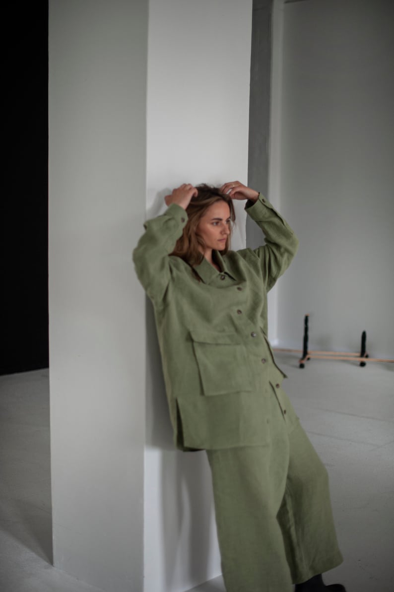K&ouml;nnte beinhalten: Eine Frau tr&auml;gt einen gr&uuml;nen Leinen-Jumpsuit mit einem Hemdkragen und einer gro&szlig;en Tasche auf der Vorderseite. Der Jumpsuit hat eine lockere Passform und ist mit einem l&auml;ssigen Look gestylt.