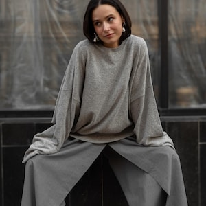 May include: A light gray long-sleeve crewneck sweater with a relaxed fit and dropped shoulders, paired with wide-leg trousers in a darker shade of gray. The sweater features a soft, textured knit fabric, while the trousers have a structured drape.