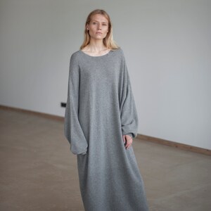 May include: A gray oversized sweater dress with long sleeves and a relaxed fit. The dress is made of a soft, comfortable material and has a simple, elegant design.
