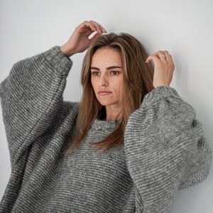 May include: A woman wearing a gray oversized knitted sweater with a loose fit and long sleeves.