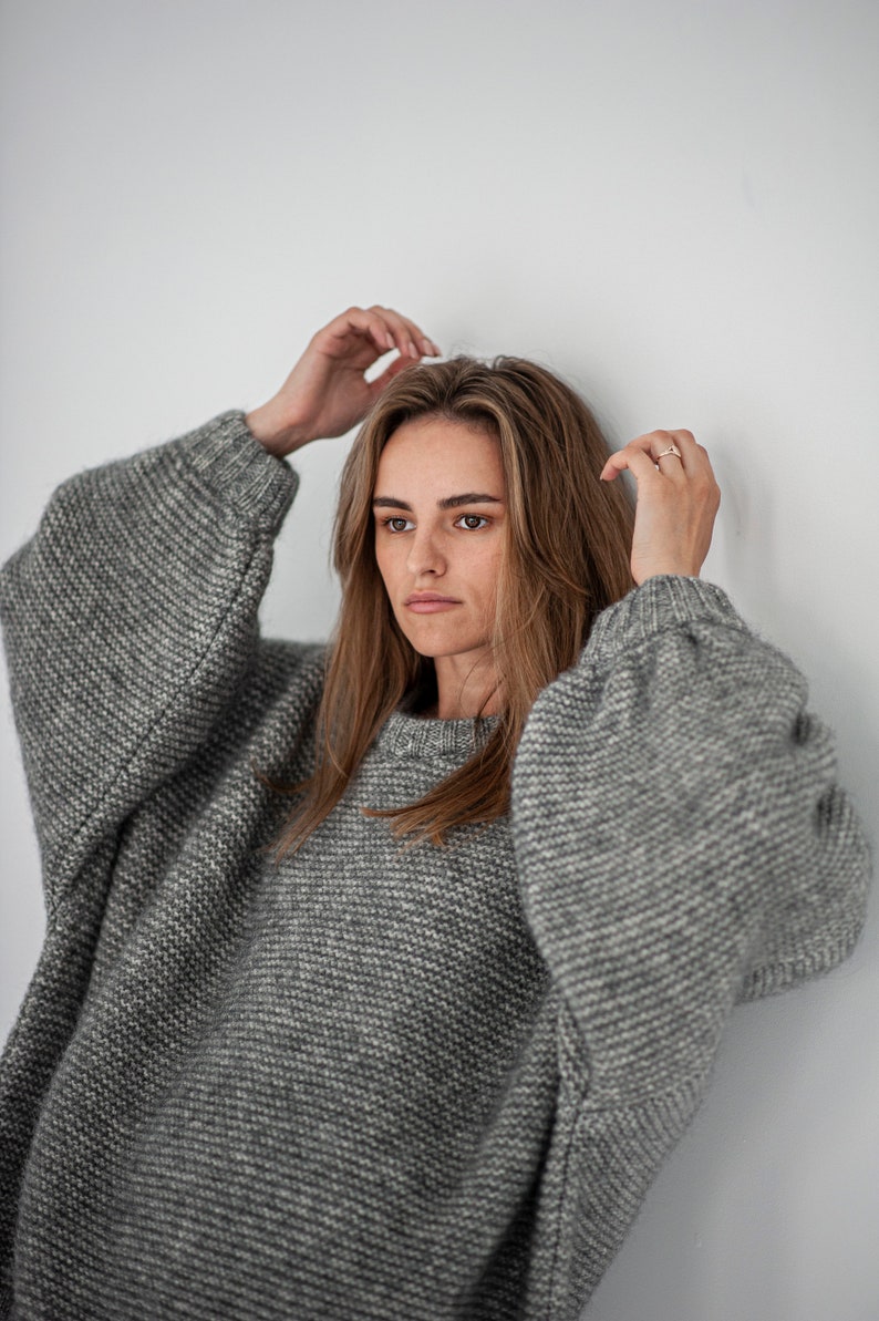 May include: A woman wearing a gray oversized knitted sweater with a loose fit and long sleeves.
