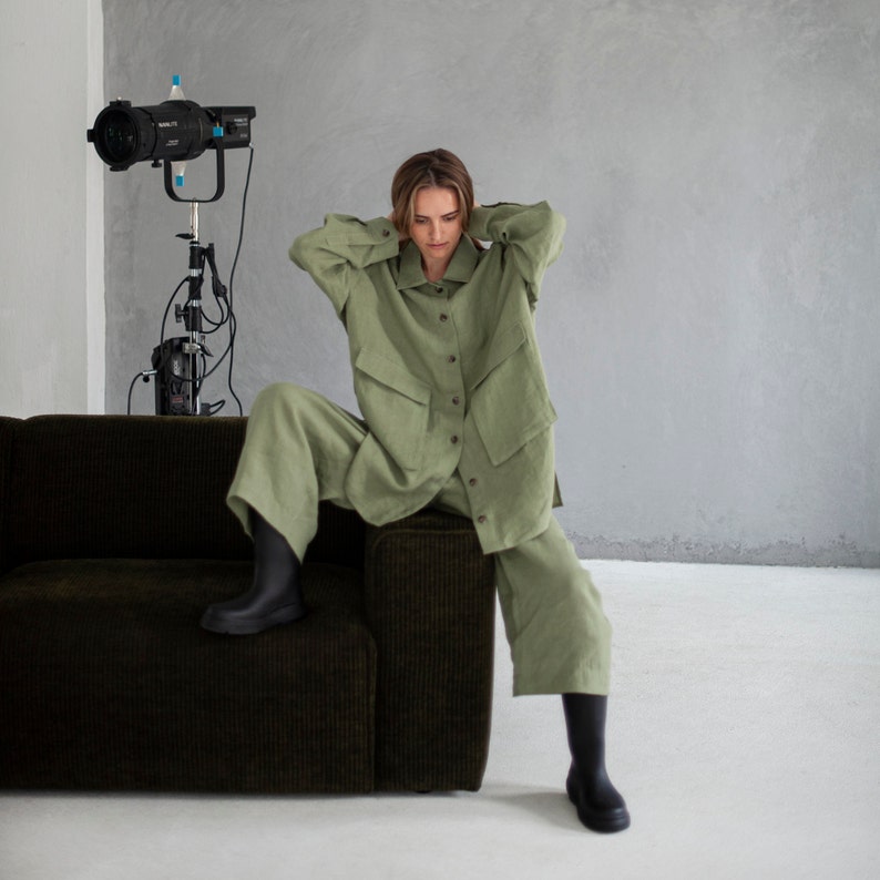 K&ouml;nnte beinhalten: Eine Person in einem gr&uuml;nen Leinenhemd und einer gr&uuml;nen Leinenhose sitzt auf einem braunen Cord-Sofa. Die Person tr&auml;gt schwarze Stiefel.