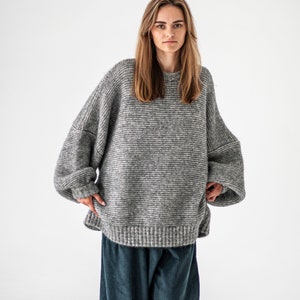 May include: A gray oversized knit sweater with long sleeves and a relaxed fit. The sweater is made of a soft, fuzzy material and has a slightly textured surface.