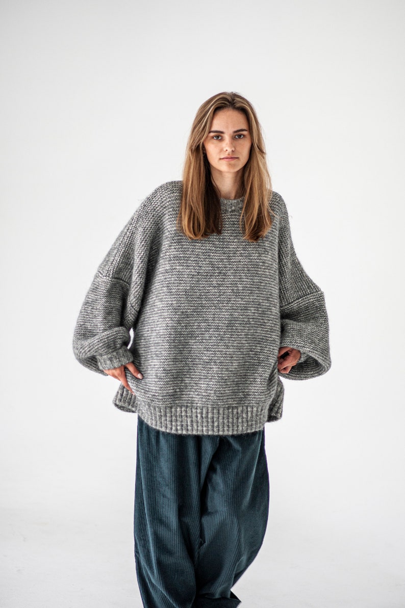 May include: A gray oversized knit sweater with long sleeves and a relaxed fit. The sweater is made of a soft, fuzzy material and has a slightly textured surface.
