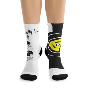 May include: A pair of white and black socks with a music-themed design. One sock features a record with a yellow label and the other sock features a microphone, a record, a record player, and a signature.