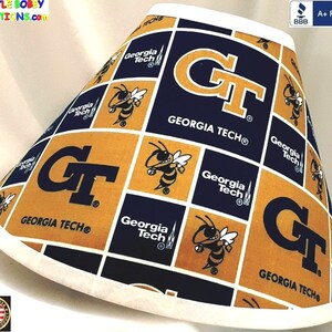 May include: A white lampshade with a gold and blue pattern featuring the Georgia Tech logo and mascot, a yellow and black bumblebee. The text "GEORGIA TECH®" is repeated throughout the pattern.