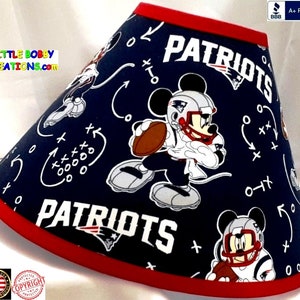 May include: Navy blue lampshade with a red trim, featuring a repeating pattern of Mickey Mouse in a football uniform and the word "PATRIOTS". White football play diagrams are scattered across the shade. The text "LITTLE BOBBY CREATIONS.com" is visible.