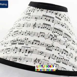 May include: A white lampshade with a black trim, featuring a musical note pattern. The lampshade has the text "LITTLE BOBBY CREATIONS.COM" printed on the bottom.