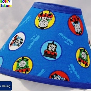May include: Blue lampshade with a Thomas the Tank Engine print. The lampshade has a blue trim and features various characters from the show.