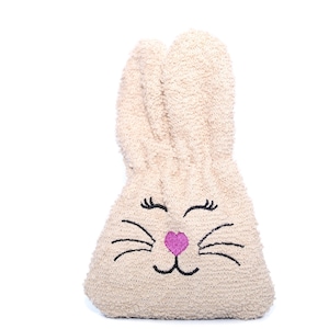 Puede incluir: Una bolsa de peluche beige con forma de conejo con ojos negros, pesta&ntilde;as, bigotes y una nariz rosa bordados.
