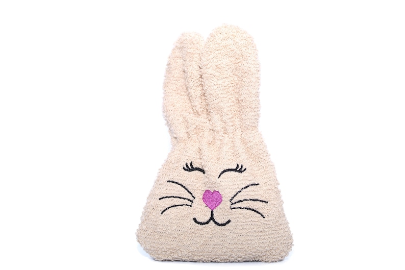 Puede incluir: Una bolsa de peluche beige con forma de conejo con ojos negros, pesta&ntilde;as, bigotes y una nariz rosa bordados.