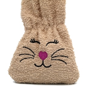 Puede incluir: Una bolsa de peluche marr&oacute;n con forma de conejo con un coraz&oacute;n rosa y bigotes y pesta&ntilde;as bordados en negro.