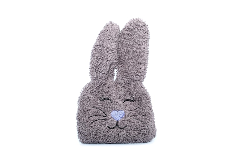 Puede incluir: Un conejito de peluche gris con ojos bordados y una nariz azul. El conejito est&aacute; hecho de un material suave y esponjoso.